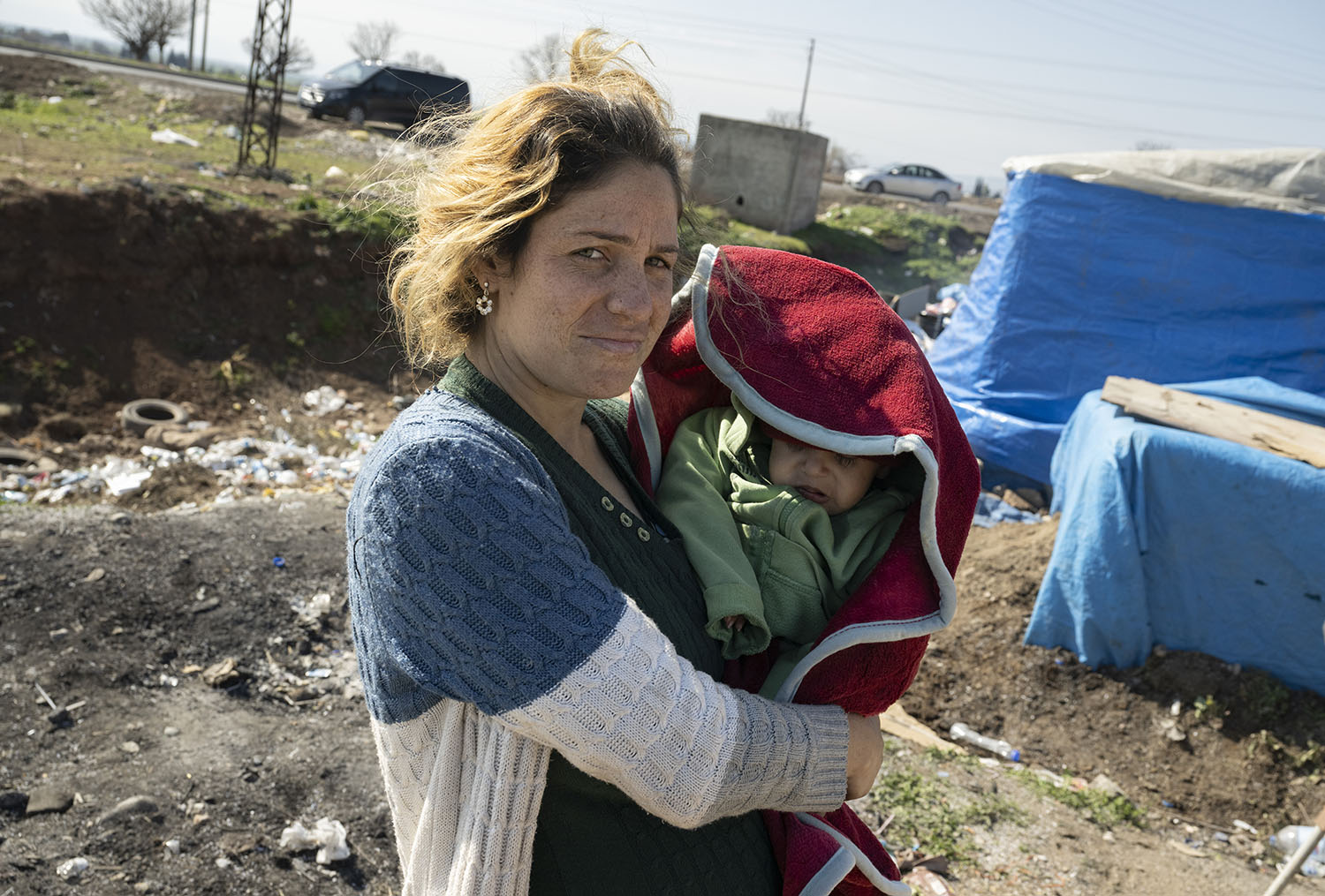 14 February 2023, Kirikhan, Türkiye: A woman carries her baby through a makeshift tent camp. (Boris Roessler/picture-alliance/dpa/AP Images)