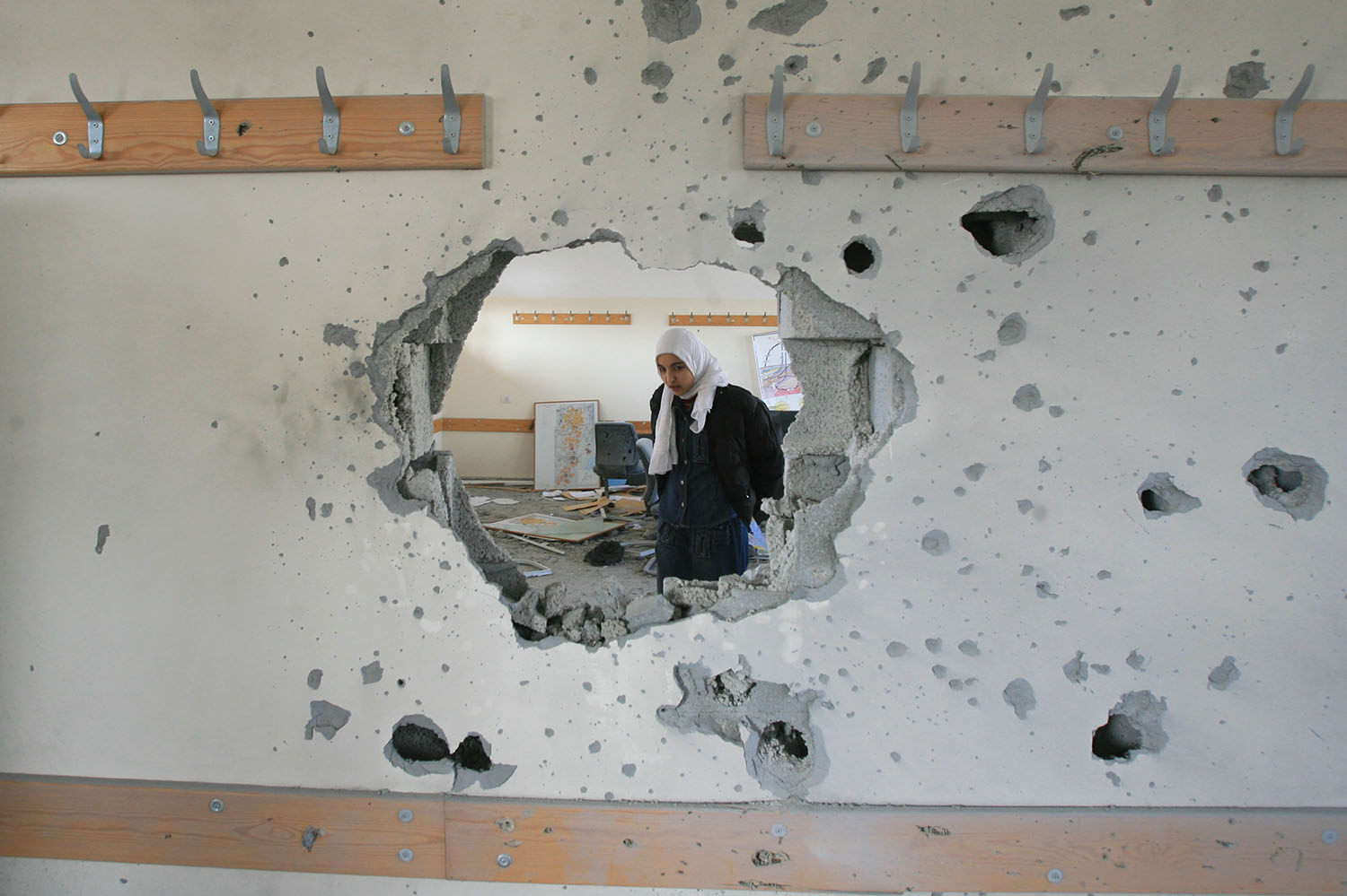 Muslim girl walks through war damaged school building.