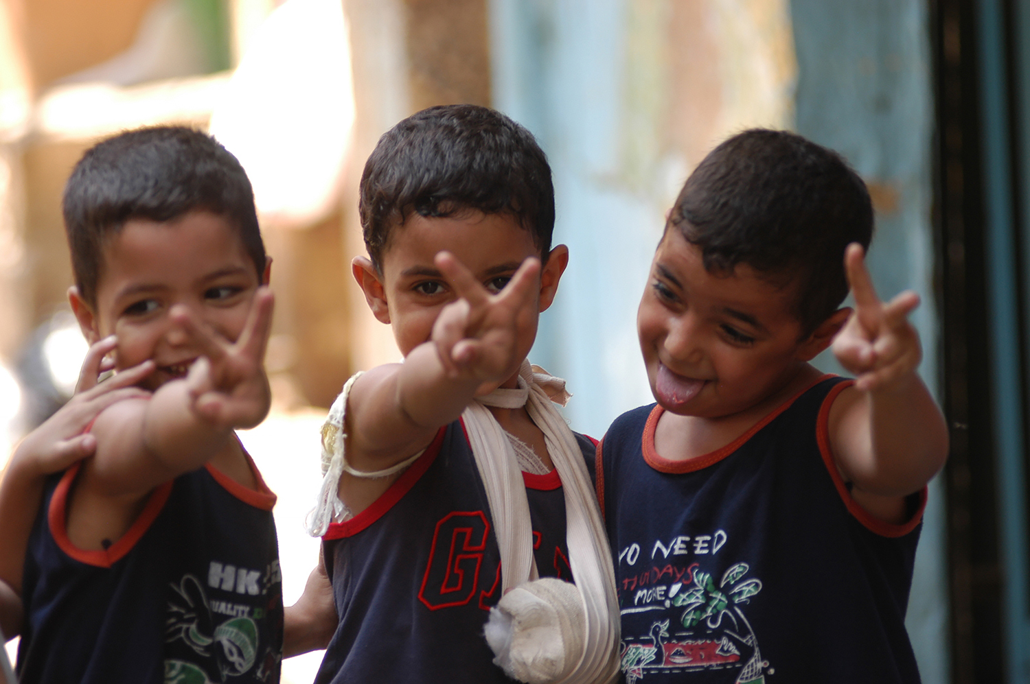 Smiling refugee boys hold hand peace signs.