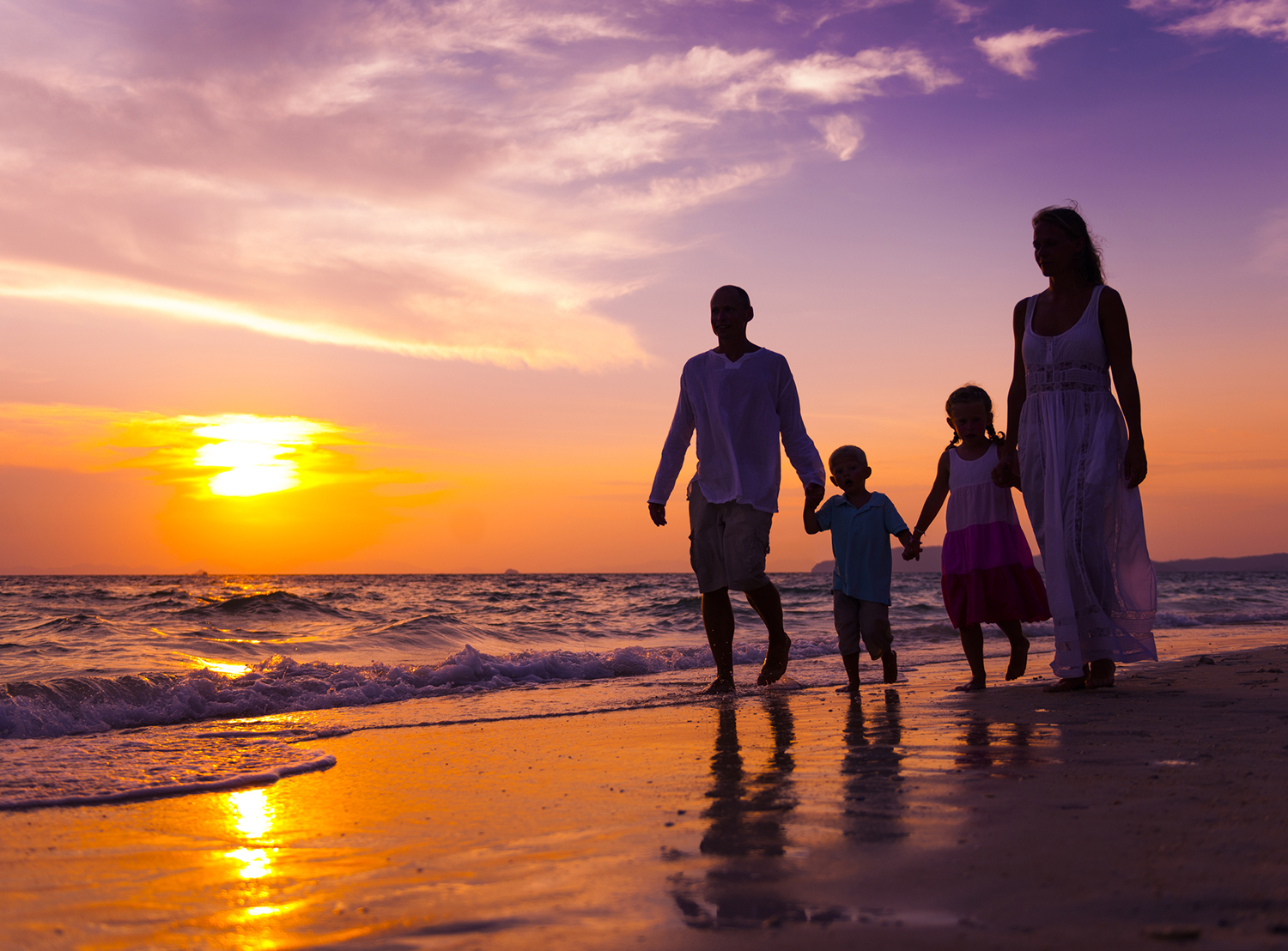 Mother, father, daughter and son share a bonding experience while walking along the oceanside at sunset holding hands.