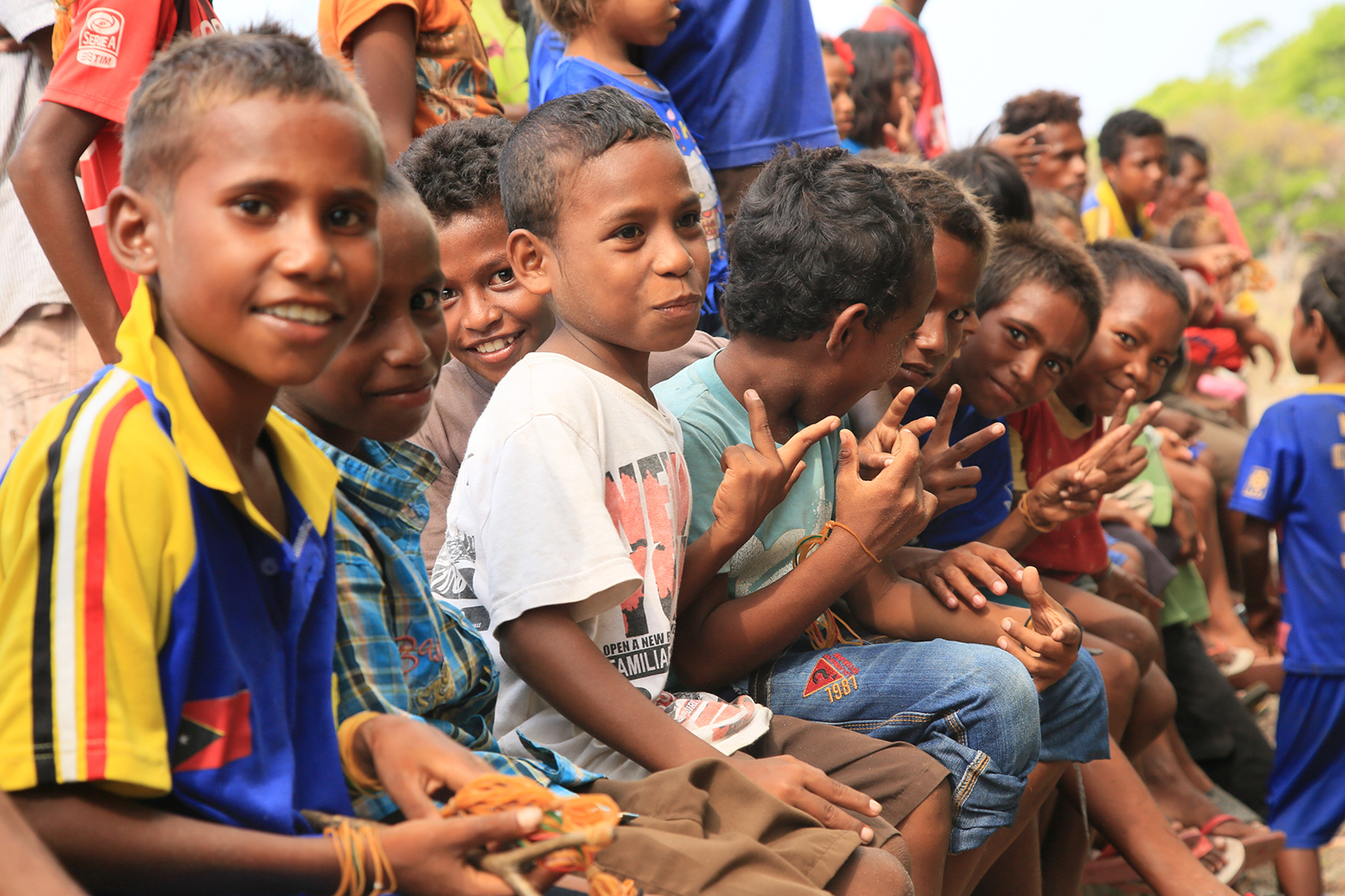 Timor Leste children sitting together hold hand peace signs.