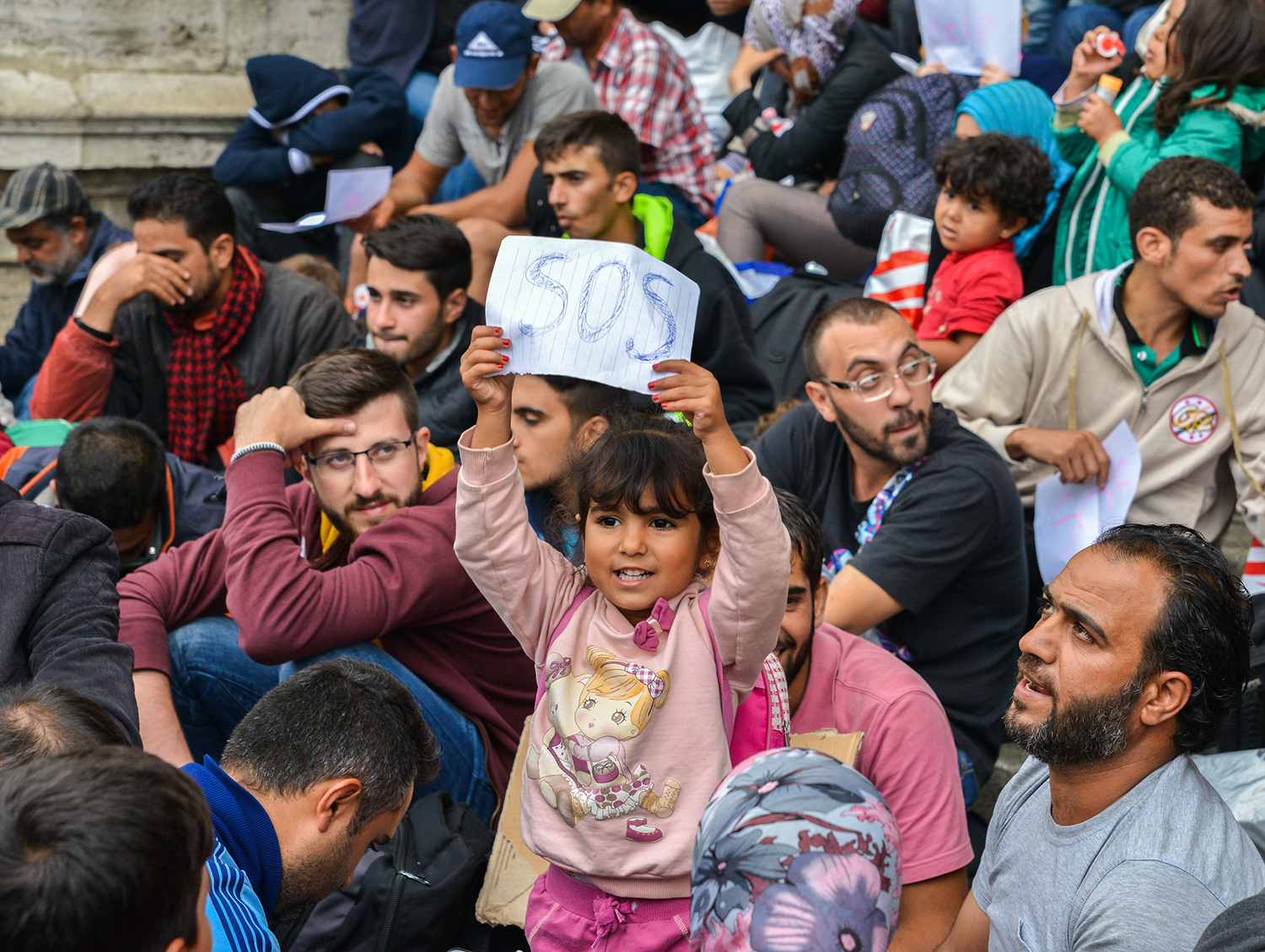 A young refugee girl holds up a SOS sign at Keleti Rail Station, Budapest, Hungary. 
