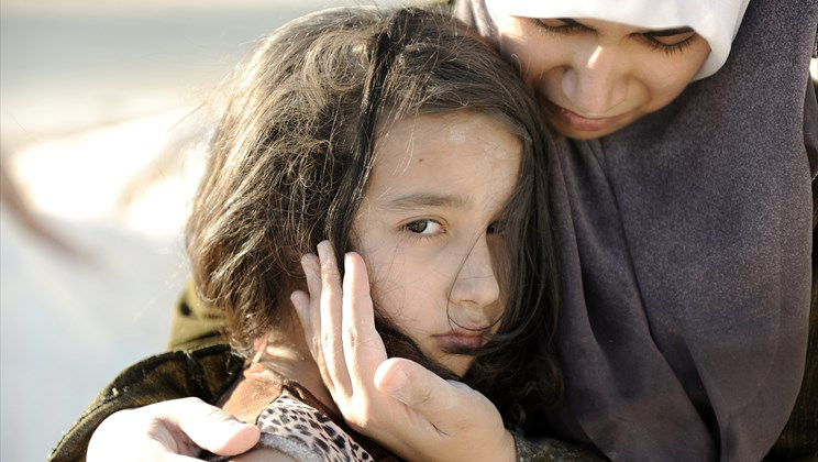 Syrian refugee mother comforts her frightened daughter.