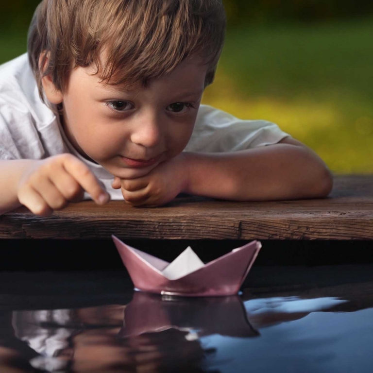 Young boy launches paper ship in a pool of water. 