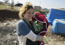 14 February 2023, Kirikhan, Türkiye: A woman carries her baby through a makeshift tent camp. (Boris Roessler/picture-alliance/dpa/AP Images)