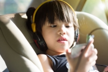 Young boy in car seat listens to a program on his mobile phone.