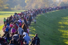Hundreds of Slovenia refugee children and families travel together across a countryside on foot.
