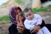 Syrian refugee mother with baby holds a hand peace sign.