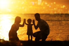 Mother and father share a bonding experience with their young child by holding hands on an ocean beach at sunset. 