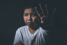 Asian boy at high risk of being bullied, trafficked and abused signals "Stop" with his hand. 
