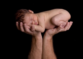 Newborn lifted in father's hands.